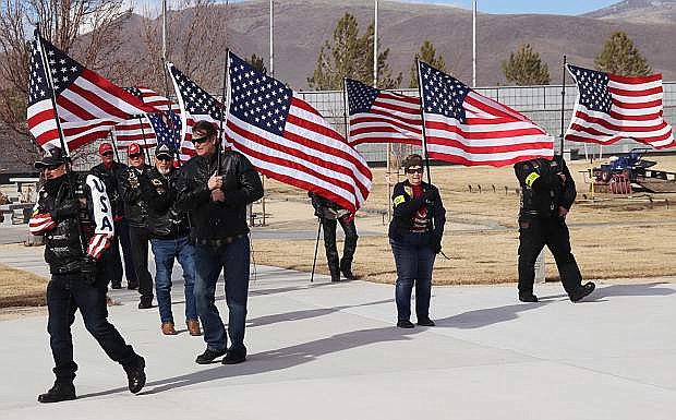 Patriot Guard Riders carry numerous U.S. flags as winds whipped the Northern Nevada Veterans Memorial Cemetery before a ceremony began to honor seven veterans.