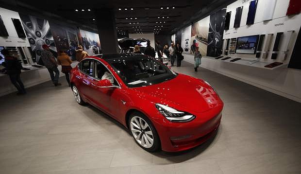 FILE - In this Feb. 9, 2019, file photograph, buyers look over a Model 3 in a Tesla store in Cherry Creek Mall in Denver. Tesla is shifting all of its sales from stores to the internet, saying the move is needed to cut costs so it can sell the mass-market Model 3 for a starting price of $35,000. The Palo Alto, California, company announced the change Thursday, Feb. 28. (AP Photo/David Zalubowski, File)