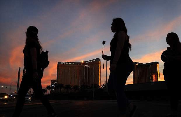 FILE - In this April 1, 2018, file photo, people carry flowers as they walk near the Mandalay Bay hotel and casino during a vigil for victims and survivors of a mass shooting in Las Vegas. Casino giant MGM Resorts is telling federal regulators it thinks it might pay up to $800 million to settle liability lawsuits stemming from the October 2017 mass shooting that became the deadliest in modern U.S. history. (AP Photo/John Locher, File)