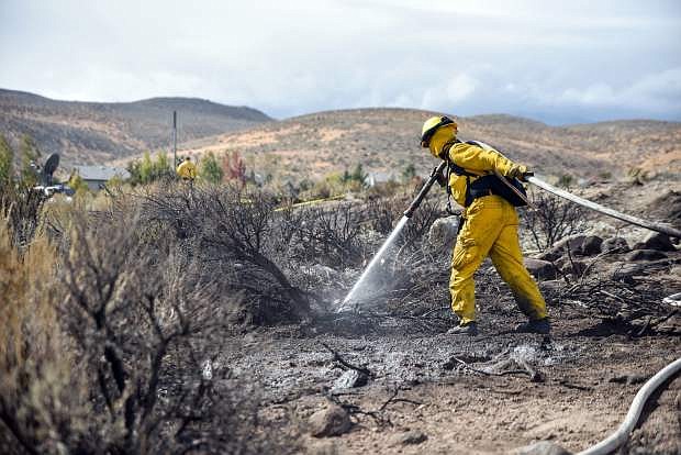 FILE - In this Oct. 14, 2016, photo, a firefighter hoses down the area on Mount Rose Highway and Edmonton Drive.