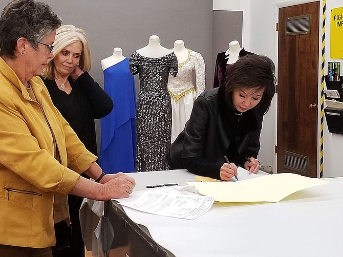 First Lady Kathy Sisolak signs a deed of gift as Jan Loverin, curator of clothing and textiles, and former First Lady Dema Guinn look on.