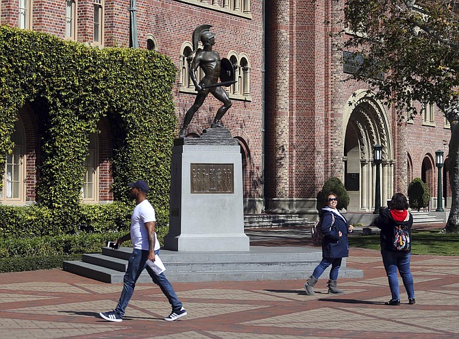 FILE - In this March 12, 2019, file photo, people pose for photos in front of the iconic Tommy Trojan statue on the campus of the University of Southern California in Los Angeles. The death of nine students since classes began a little more than two months ago has left students and administrators at the University Southern California shaken and seeking answers. The Los Angeles Times reports the latest death was discovered Monday, Nov. 11, 2019, when the body of a 27-year-old student was found in an off-campus apartment. (AP Photo/Reed Saxon, File)