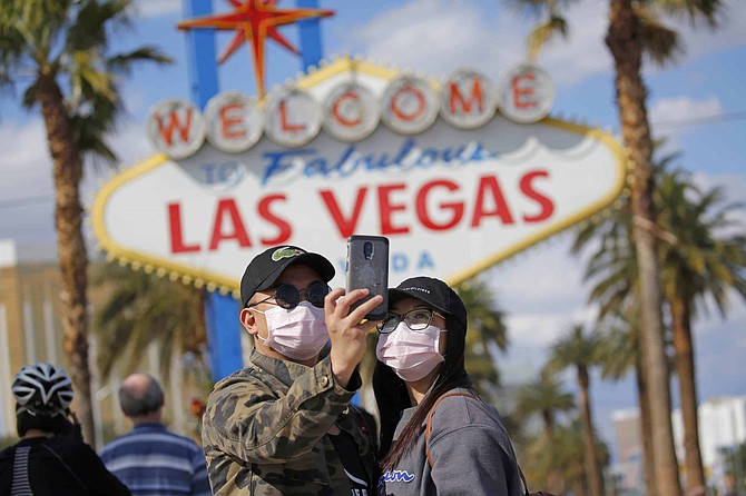 FILE - In this March 21, 2020 file photo, a couple wearing face masks take a selfie at the &quot;Welcome to Fabulous Las Vegas Nevada&quot; sign amid a shutdown of casinos along the Las Vegas Strip due to coronavirus in Las Vegas. The emerging coronavirus pandemic has spurred a lawsuit by a Las Vegas attorney with a background in big cases, who is seeking compensation from the Chinese government for more than 32 million small U.S. businesses that have lost income and profits as a result of the outbreak. Eglet seeks class-action status and said Tuesday, March 24, 2020 he believes damages for Chinese &quot;reckless&quot; and &quot;negligent&quot; conduct could be in the trillions of dollars. They seek compensation from the government of China. 