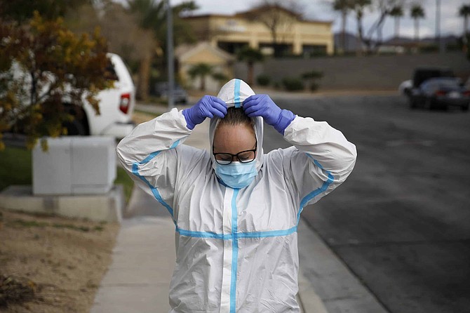 Paramedic Chelsea Monge of Ready Responders removes personal protective equipment after making a house call for a possible coronavirus patient Friday, April 10, 2020, in Henderson, Nev. Ready Responders is a group that makes house calls for non emergencies and will connect the patient with a doctor via a telehealth service. Monge estimates that about half of calls to the group in the past month have been for flu-like symptoms. (AP Photo/John Locher)