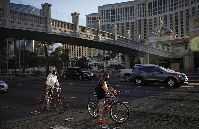 People wearing masks pause while riding bicycles along the Las Vegas Strip devoid of the usual crowds as casinos and other business are shuttered due to the coronavirus outbreak, Tuesday, April 14, 2020, in Las Vegas. 
