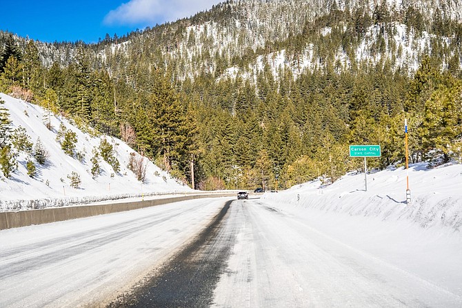 Driving on an ice and snow covered road through the Sierra mountains on a sunny day; Carson City road sign on the right; Nevada