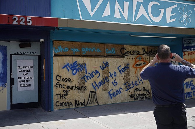 A man takes a picture of a business closed and boarded due to the concerns of the new coronavirus Wednesday, March 25, 2020, in Las Vegas.  Gov. Steve Sisolak on Tuesday night issued an emergency order banning gatherings of more than 10 people in the state indoors or outdoors, a more aggressive move to try to slow the spread of the coronavrius. 