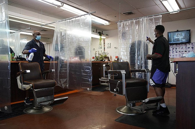 Pat Renfro, left, and Dolla Green clean their chairs between customers at A Cut Above the Rest barber shop, Saturday, May 9, 2020, in Las Vegas. Saturday was the first day restaurants, salons and other nonessential businesses were allowed to start reopening after restrictions were imposed seven weeks earlier to help stop the spread of the new coronavirus. 