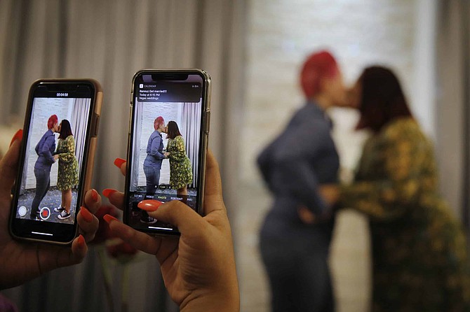 Cynthia Sanchez takes video and pictures as her sister Jennifer Escobar, right, and Luz Sigman kissing during their wedding ceremony at Vegas Weddings, Friday, May 8, 2020, in Las Vegas. The couple, from San Francisco, couldn&#039;t find a county clerk&#039;s office that would issue a wedding license closer to the Bay Area so they decided to make the 11-hour drive to Las Vegas. 