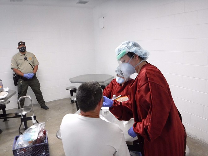 A NDOC nurse tests an offender for COVID-19 under the watchful eye of a correctional officer.