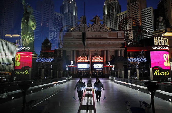 FILE - In this April 18, 2020, file photo, a lone worker wearing a mask cleans a pedestrian walkway devoid of the usual crowds as casinos and other business are shuttered due to the coronavirus outbreak in Las Vegas. Cards will be cut, dice will roll and jackpots jingle when casinos in Las Vegas and Nevada begin reopening at 12:01 a.m. on Thursday, June 4, 2020. There will be big splashes, even amid ongoing unrest, and big hopes for recovery from an unprecedented and expensive closure prompted by the coronavirus pandemic. 