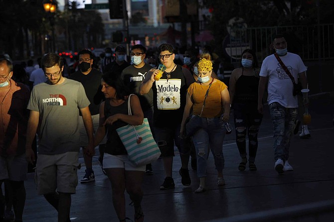FILE - In this Saturday, July 4, 2020 file photo people, some clad in masks as a precaution against coronavirus, walk along the Las Vegas Strip on the Fourth of July in Las Vegas. Nevada officials say a record high in the daily number of positive COVID-19 tests in the state may be the result of people failing to wear masks and keep distances apart during the Independence Day holiday. 