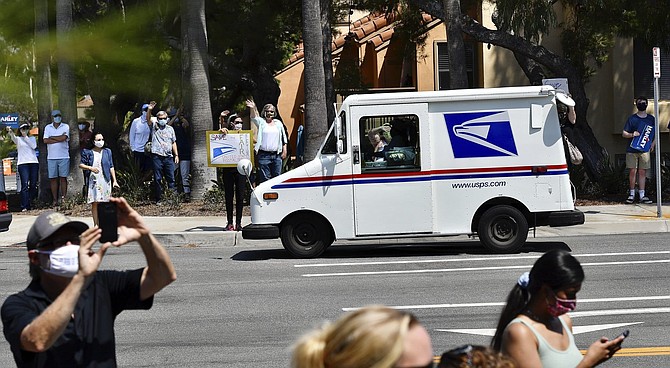 A postal carrier drives past protesters during a rally against changes to the United States Postal Service, in Newport Beach, Calif., Tuesday, Aug., 18, 2020. Facing mounting public pressure and a crush of state lawsuits, President Donald Trump&#039;s new postmaster general announced Tuesday he is halting some operational changes to mail delivery that critics blamed for widespread delays and warned could disrupt the November election.(Jeff Gritchen/The Orange County Register via AP)