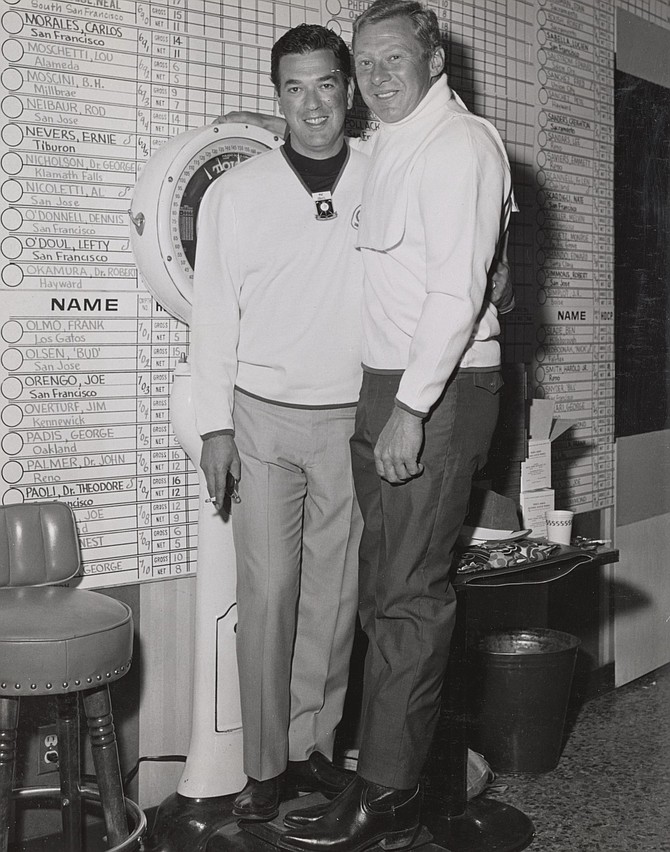 Mal Alberts and Jackie Jensen wearing white sweaters and standing in front of the wall with the list of players participating in the Nugget Golf Classic in 1967.