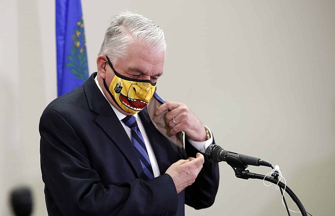 Nevada Governor Steve Sisolak removes an outer face mask during a news conference at the Grant Sawyer State Building in Las Vegas, Tuesday, Sept. 29, 2020. The yellow face mask is themed after the Vegas Golden Knights&#039; mascot Chance the Golden Gila Monster. The governor provided updates on Nevada&#039;s COVID-19 response efforts and adjustments to current capacity limits on gatherings. (Steve Marcus/Las Vegas Sun via AP, Pool)