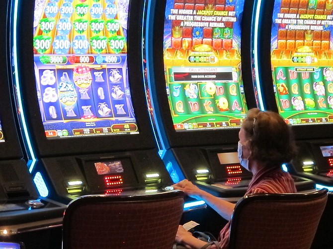 In this July 2, 2020 photo, a woman plays a slot machine at the Golden Nugget casino in Atlantic City N.J. Gambling companies in the U.S. are increasingly bringing different forms of gambling together, including sports betting, casino gambling, internet gambling and daily fantasy sports, and partnering with media companies as they seek to increase revenue. (AP Photo/Wayne Parry)