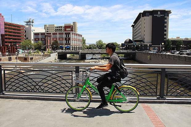 A man rides a Lime bike along the Truckee River in downtown Reno in June 2018.