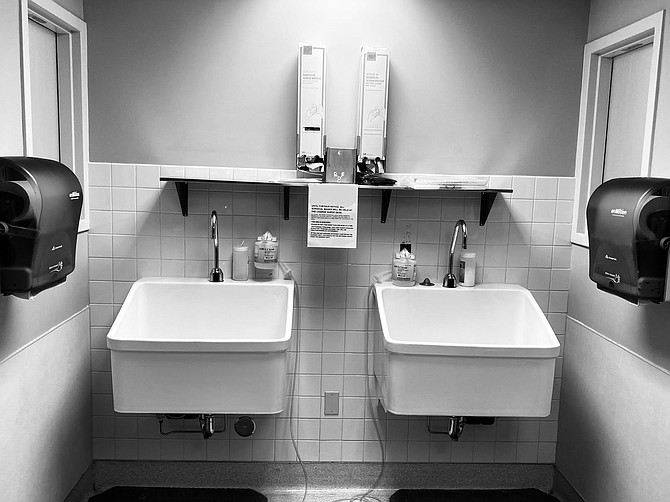 Sinks seen at a local hospital with a sign directing health care workers to the charge nurse&#039;s desk for masks.