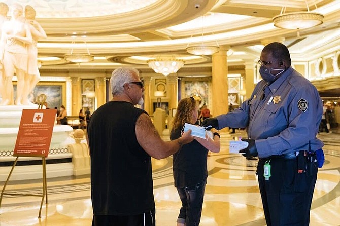 A security guard welcomes and hands a few masks to customers at Caesars Palace Las Vegas Hotel &amp; Casino after reopening June 4, 2020.